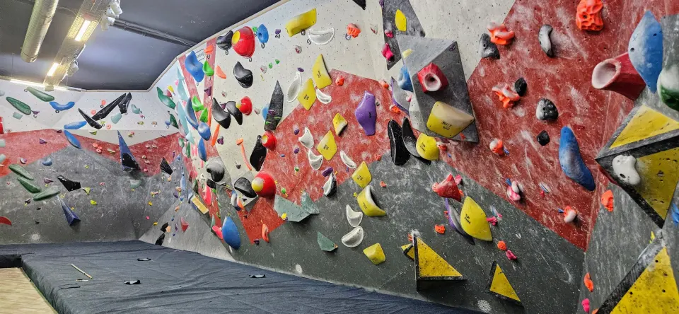 Overhanging bouldering wall with colourful holds and volumes above deep matting