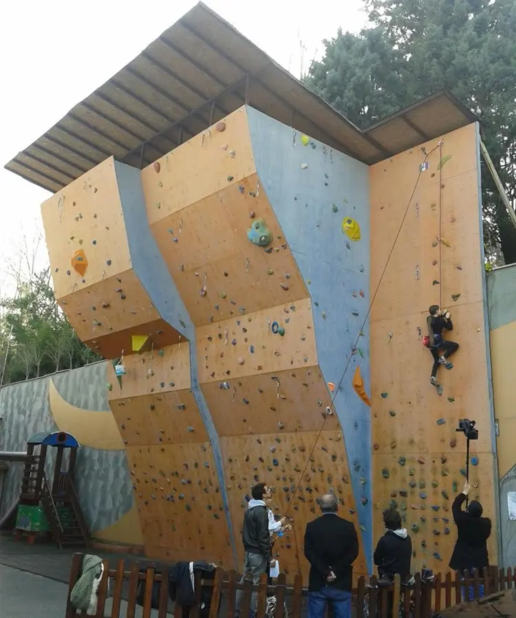 Roofed outdoor lead wall with a climber on a rope and onlookers below