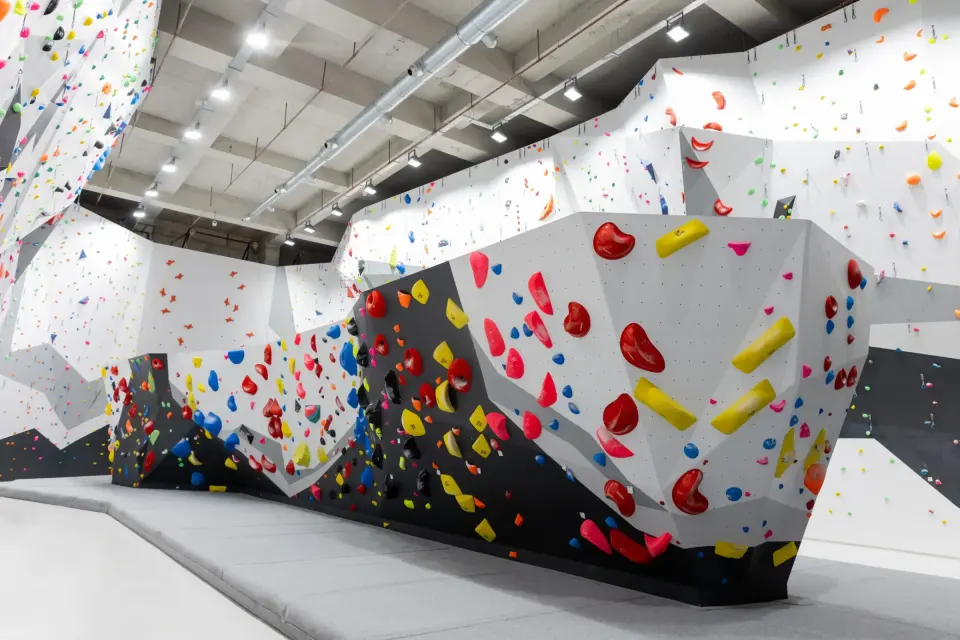 Overhanging bouldering wall with big red and yellow holds above thick grey matting