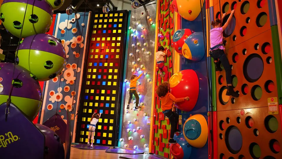 Children climbing colourful Clip 'n Climb walls, including a light-up wall and giant ball holds