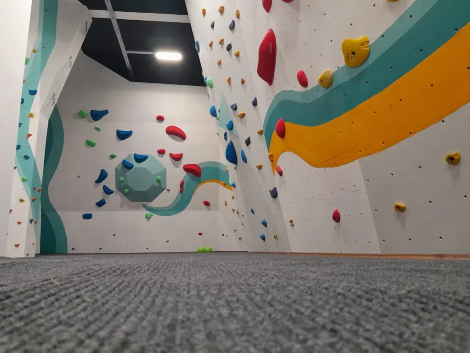 Bouldering walls with painted teal and orange stripes and a large hexagonal volume above grey matting