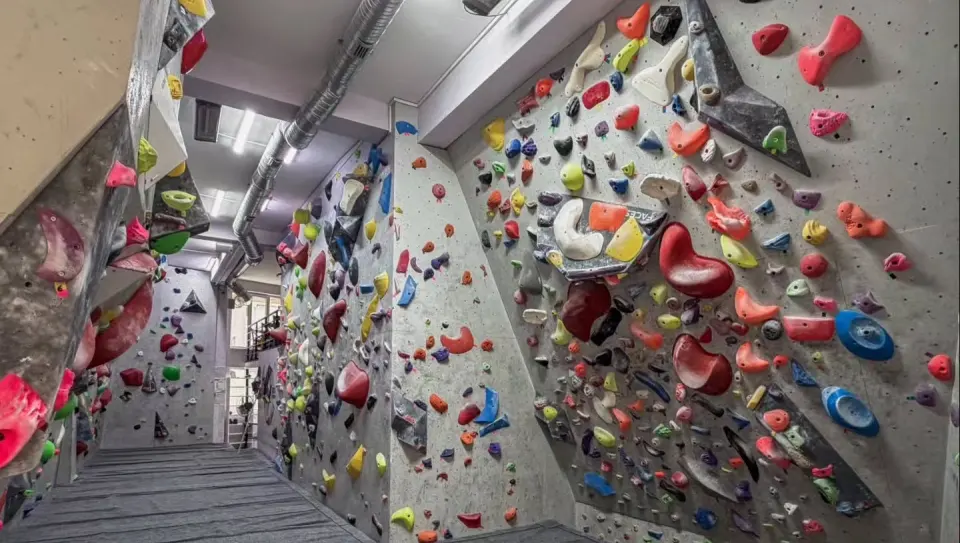 Bouldering hall with grey walls covered in colourful holds and volumes above grey matting