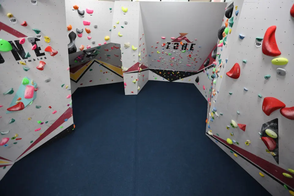 Bouldering area with angled walls, volumes and Zone logos above blue matting