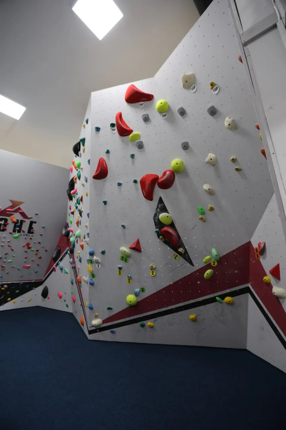 Steep bouldering wall with large red holds above blue matting