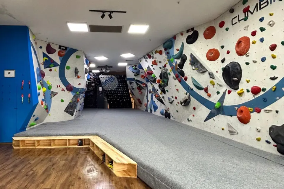 Long matted bouldering corridor between blue-and-white walls, with a MoonBoard at the far end