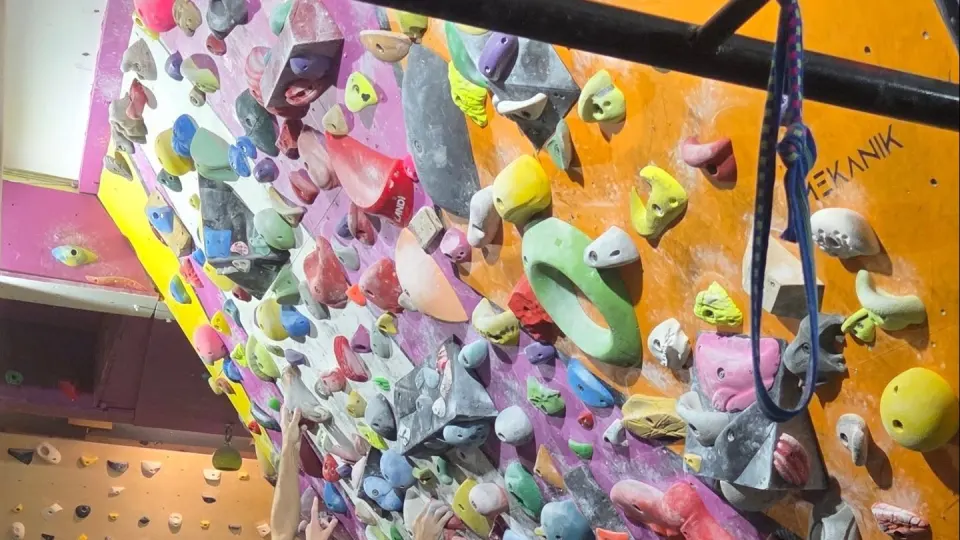 Steep bouldering wall packed with colourful holds beside an orange panel painted with the Mekanik name