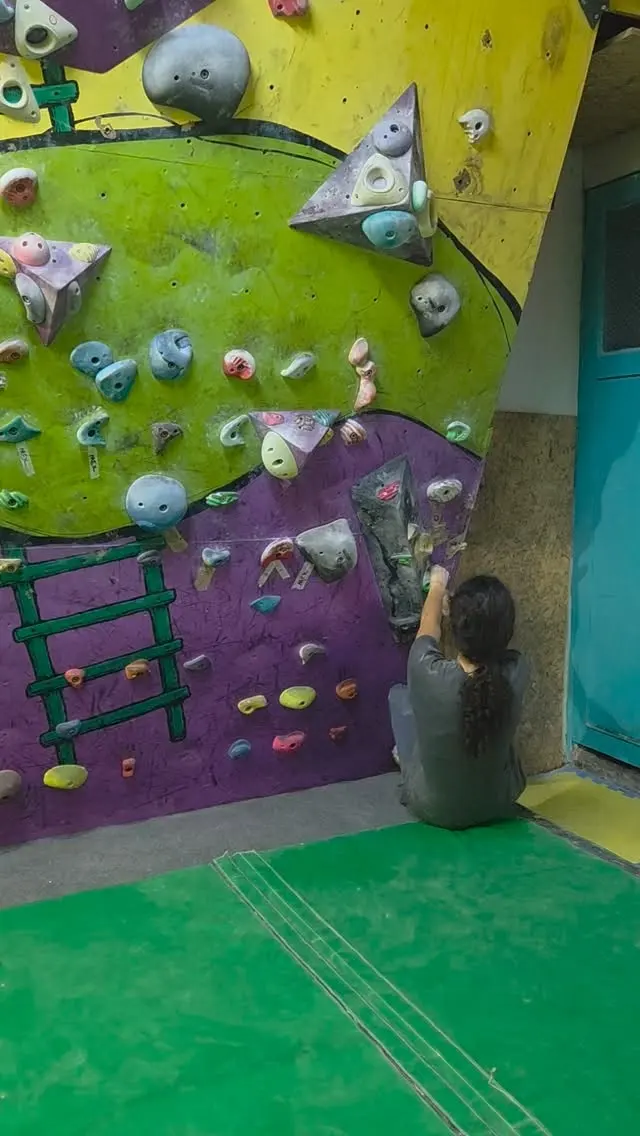 Climber starting a problem on a green and purple wall painted with a ladder