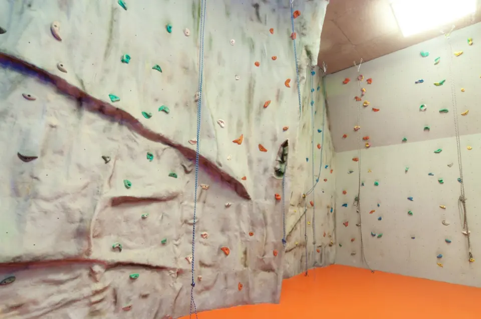 Roped climbing wall with rock-textured and flat panels above an orange floor