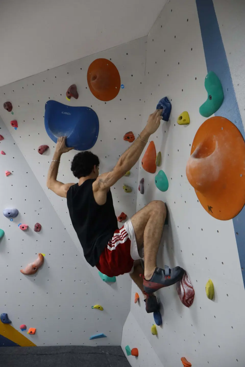 Climber reaching for a blue hold beside large orange volumes