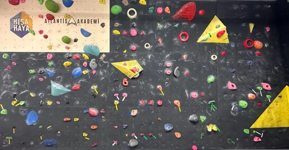 Dark bouldering wall with colourful holds, yellow volumes and the Kısakaya logo