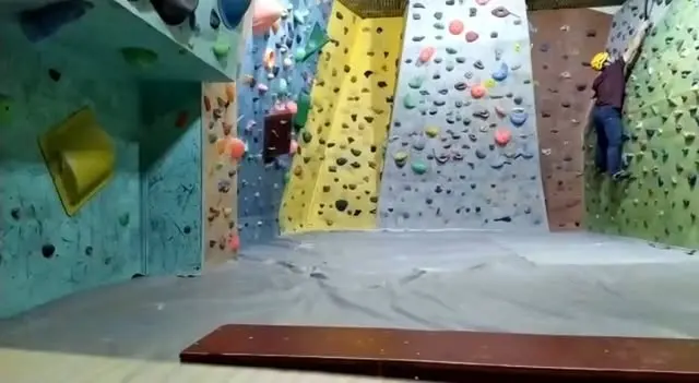 Bouldering room with teal, yellow, grey and green wall panels above grey matting