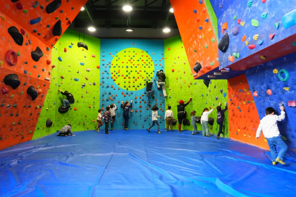 Brightly coloured bouldering walls around a blue-matted floor, with young climbers in the distance