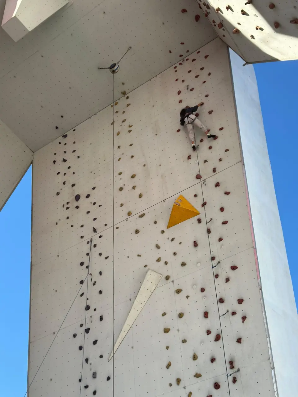 Colour-coded routes, volumes and quickdraws on the central pillar, with a climber high on the wall