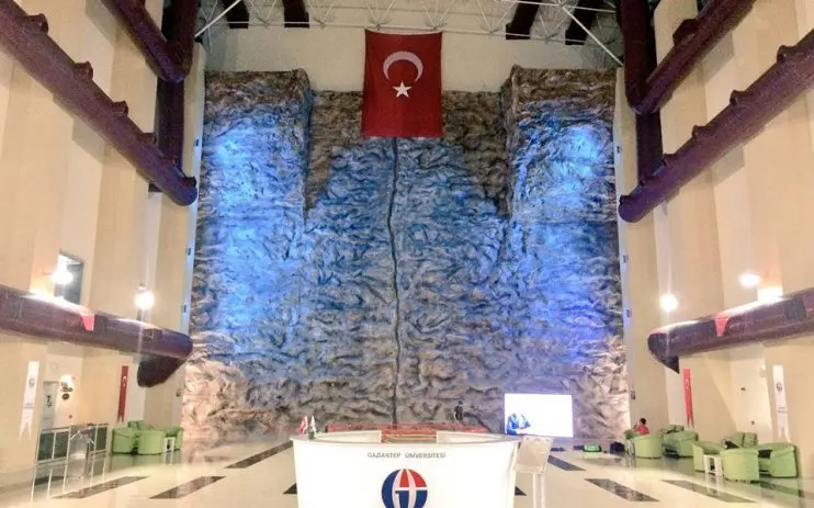 Tall sculpted rock-effect climbing wall filling the end of a bright atrium, behind the university's reception desk