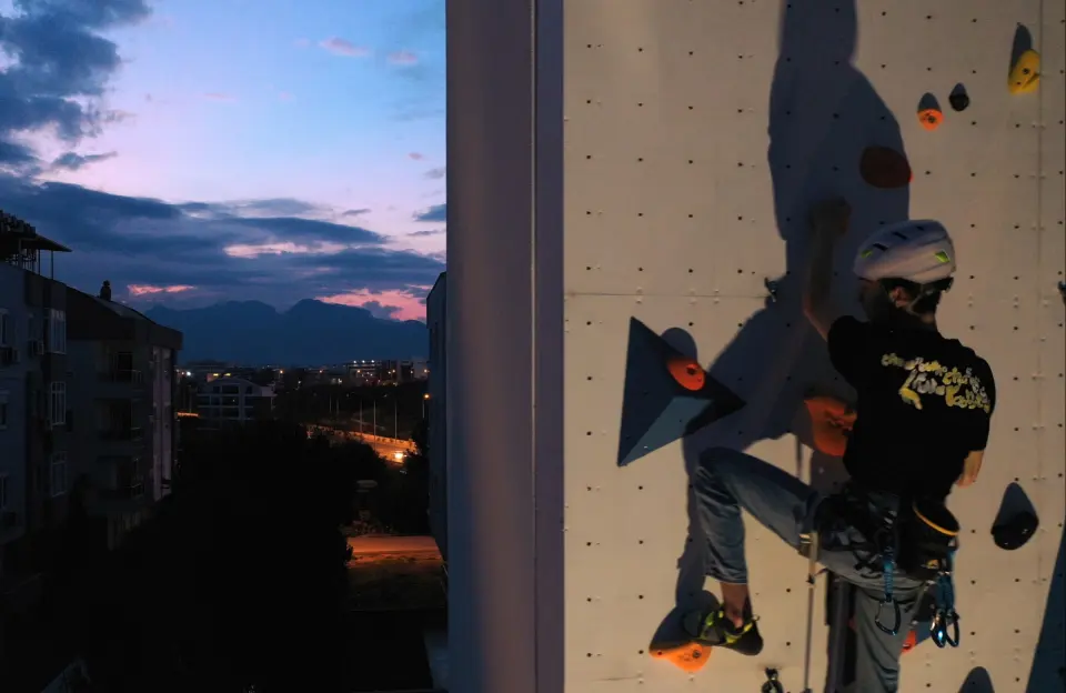 A climber on Mozaik Climbing's outdoor wall in Konyaaltı at dusk, with Antalya's mountains behind