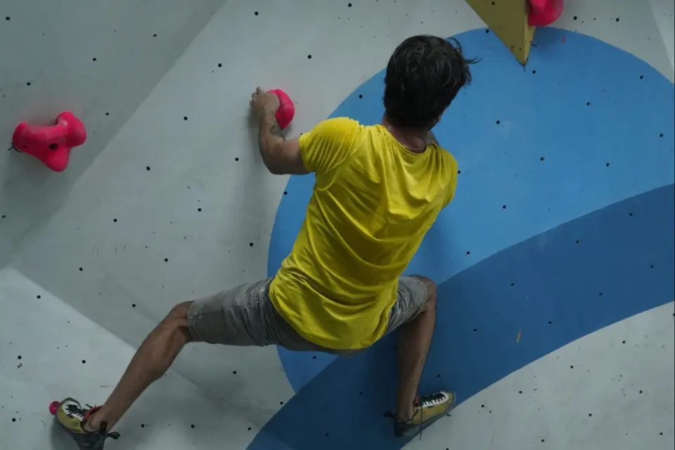 A climber in a yellow T-shirt bridging across a blue and white wall at Climbinn in Bornova