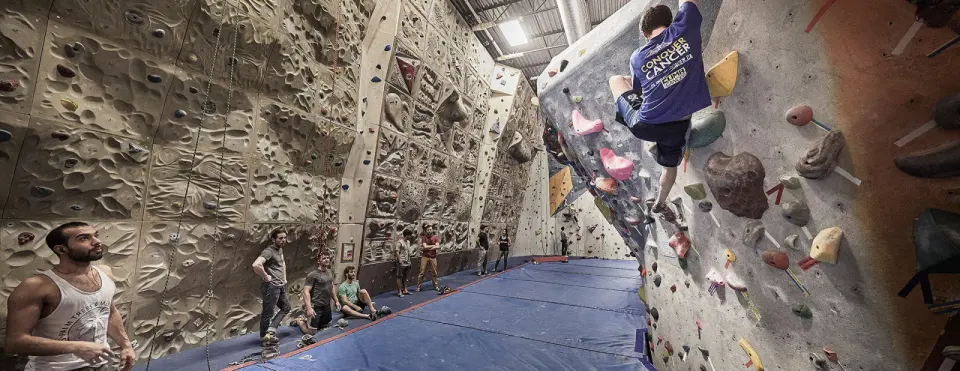 Featured rope walls and a bouldering overhang above blue matting
