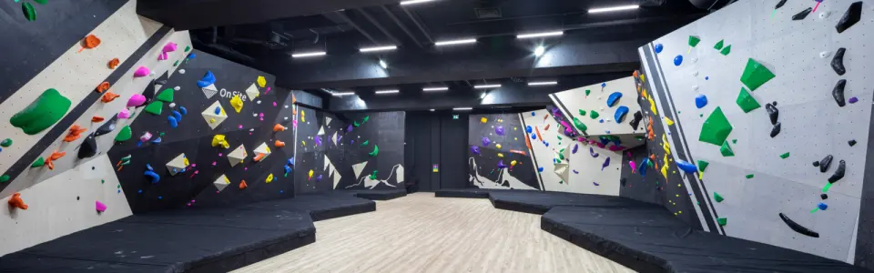 Bouldering room with angled walls around thick black mats and a pale wooden floor