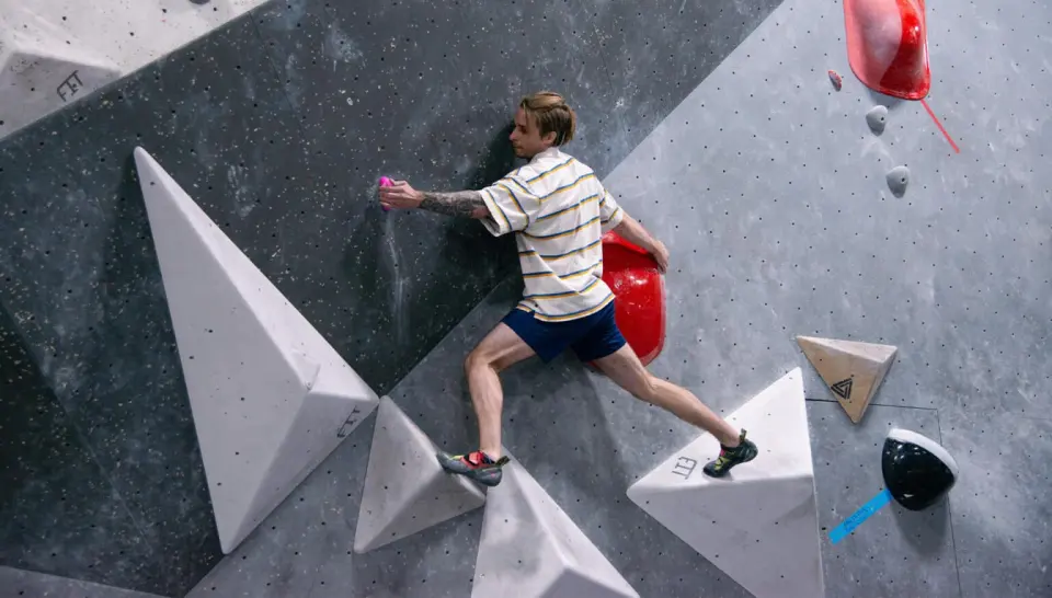 Climber bridging between white volumes on a grey bouldering wall