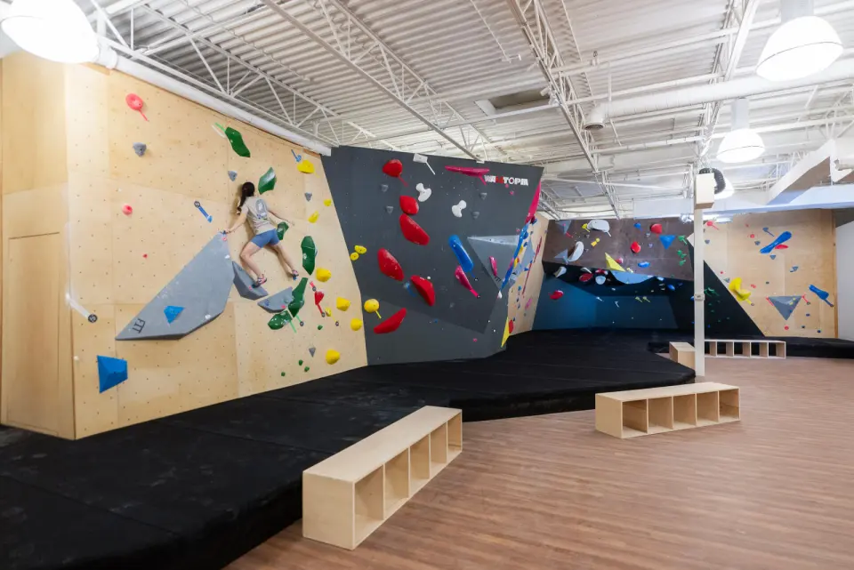 Wooden and black bouldering walls above deep black mats, with benches on a wood floor
