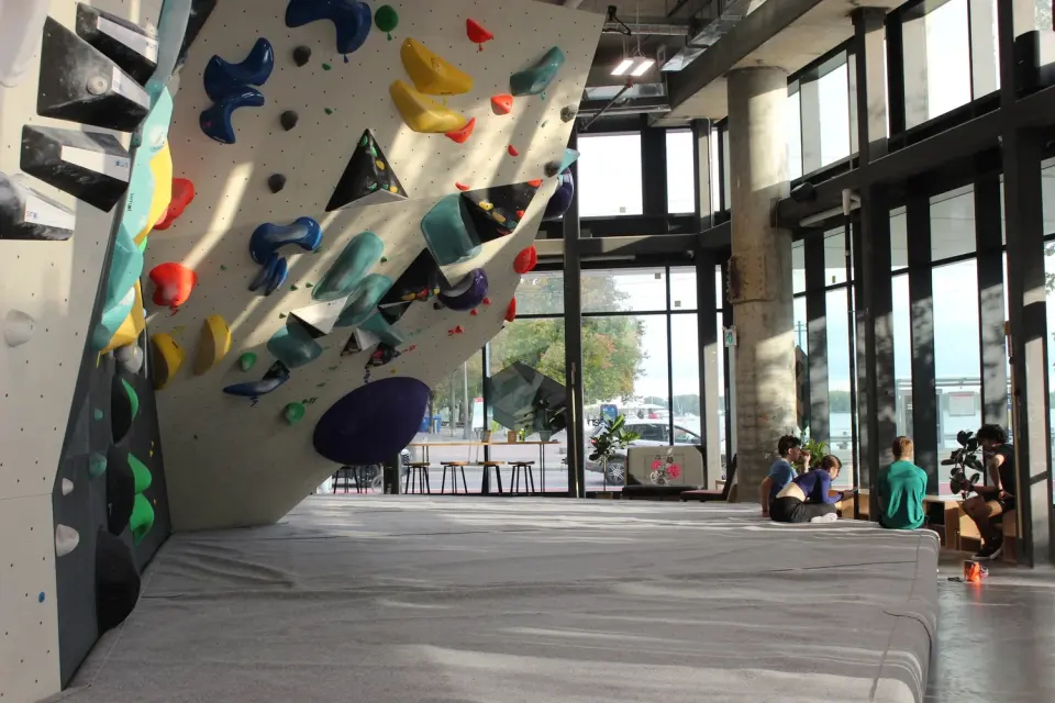 Overhanging bouldering wall above thick mats beside tall windows