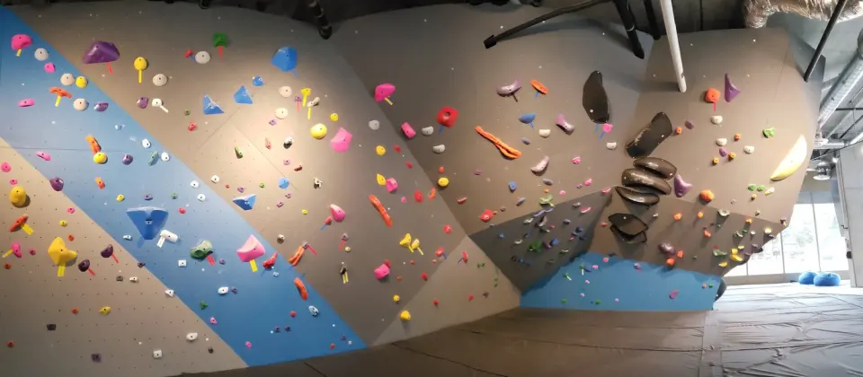 Bouldering walls with blue and grey panels and colourful holds above a padded floor
