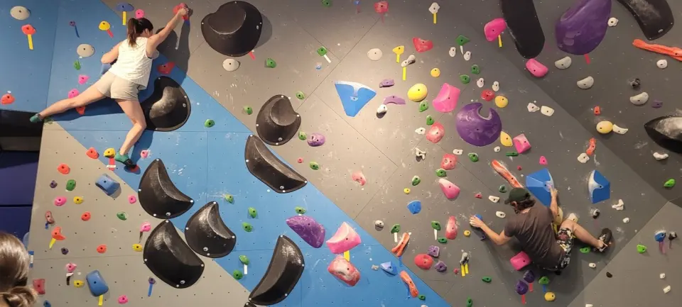 Two climbers on a bouldering wall with large black volumes