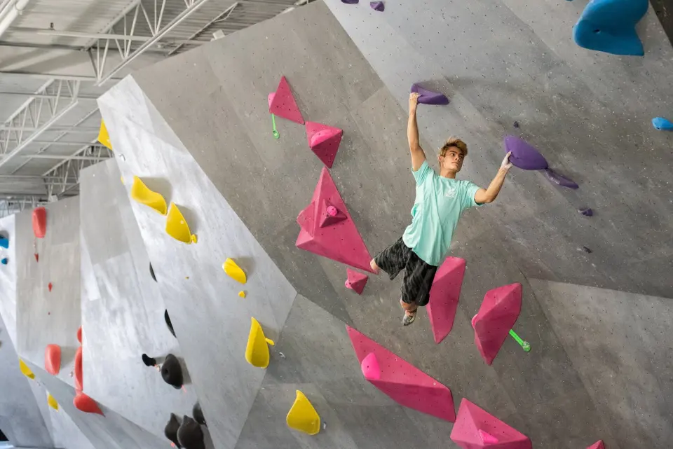 Climber hanging from large volumes on an angled competition-style wall