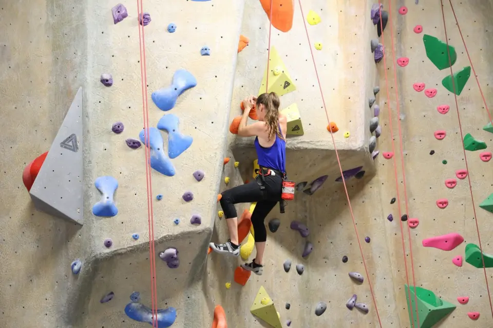 Climber on a textured top-rope wall with ropes hanging alongside