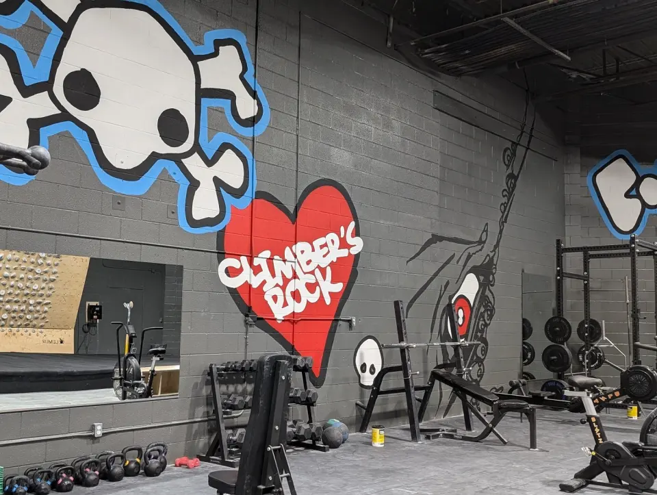 Weights area with racks, dumbbells and kettlebells beneath a painted mural