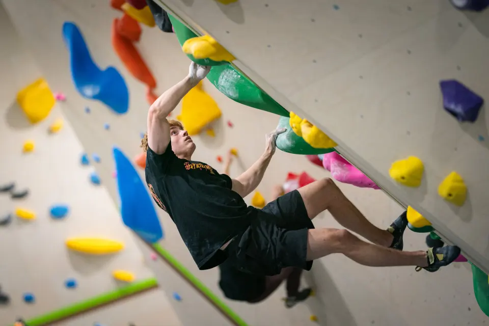 Climber pulling through large green and yellow holds on an overhanging bouldering wall