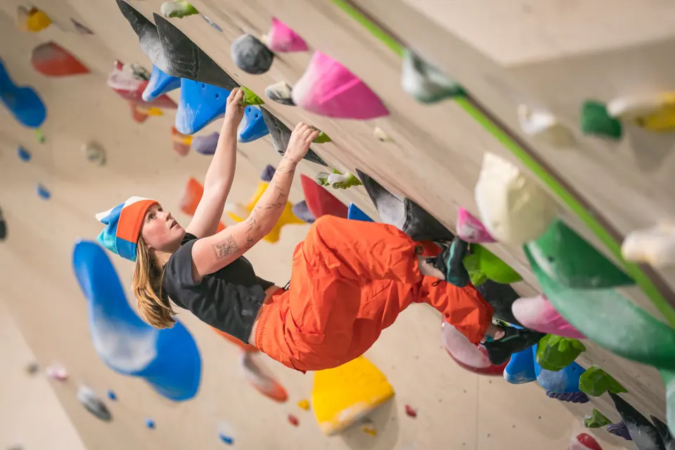 Climber on a steep wood-grain bouldering wall with colourful volumes