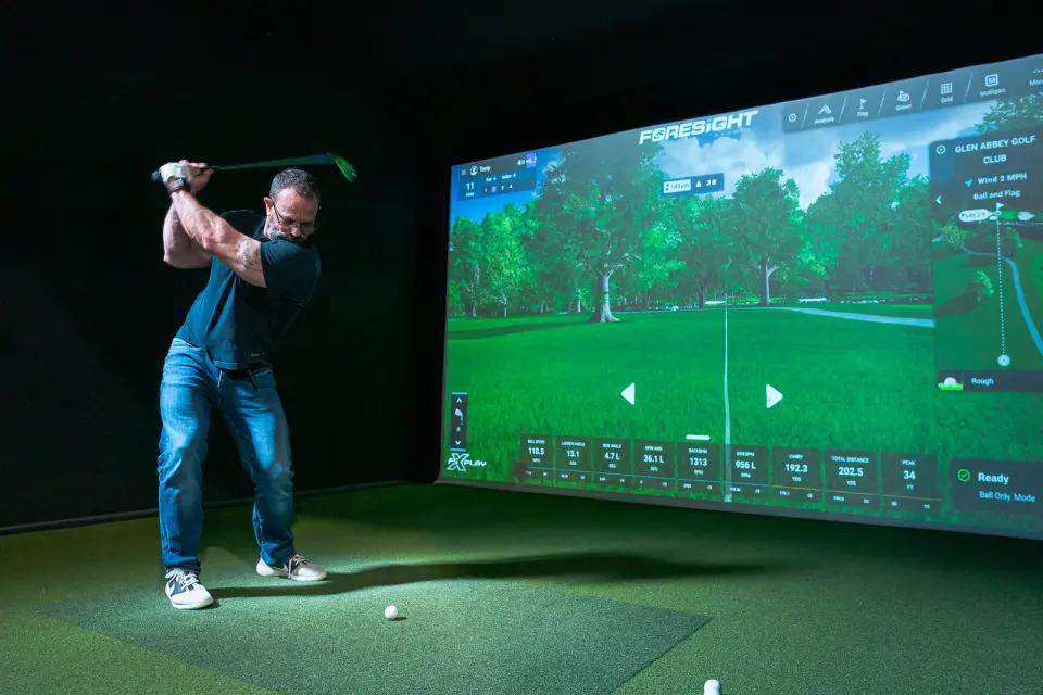 Golfer swinging in front of a golf simulator screen