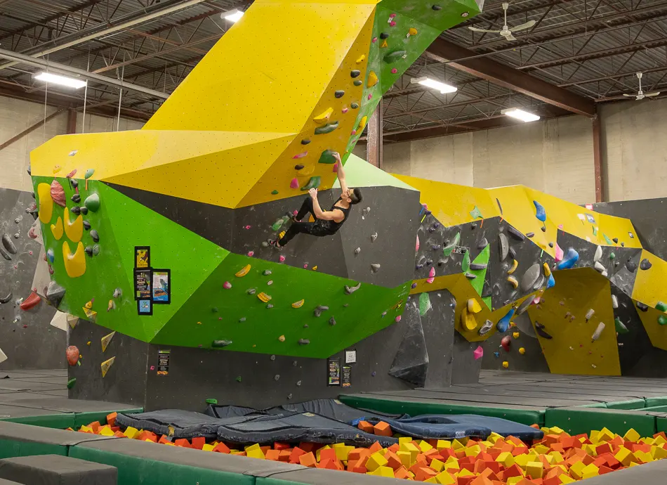 Climber on the overhanging dragon boulder above a pit of foam blocks