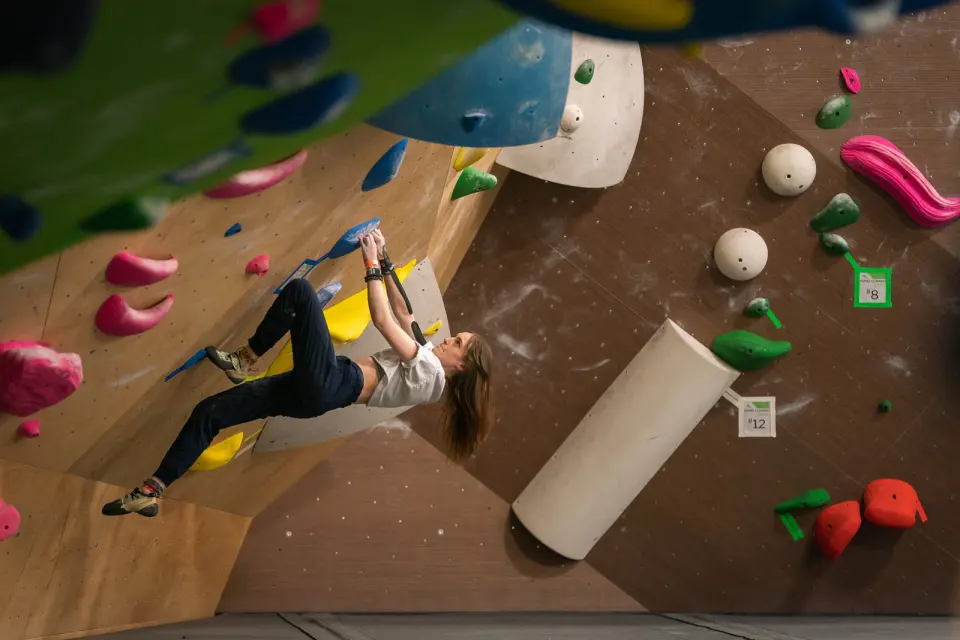 Climber on a steep wooden bouldering wall with numbered competition problems