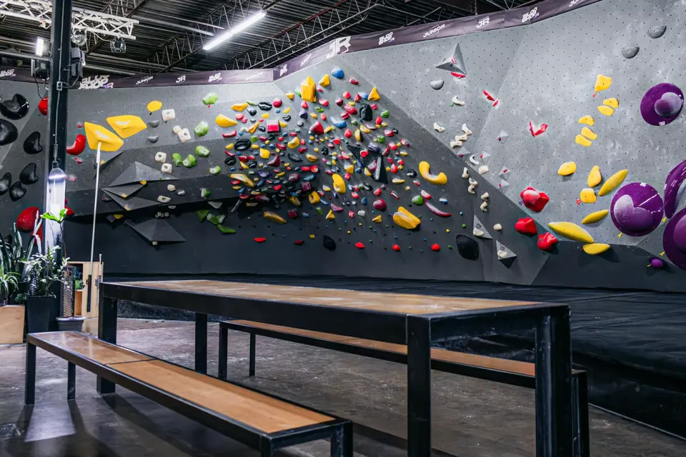 Bouldering wall dense with colourful holds behind wooden benches