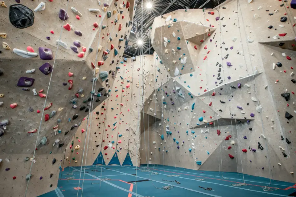 Tall roped climbing walls with ropes hanging over a blue floor