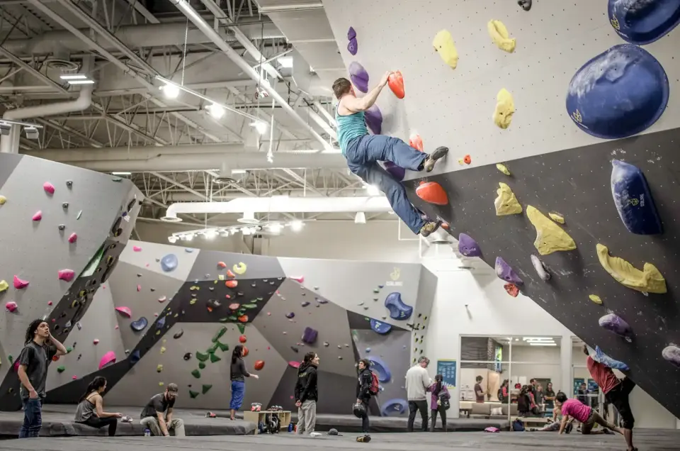 Climber on an overhanging boulder in a busy bouldering hall