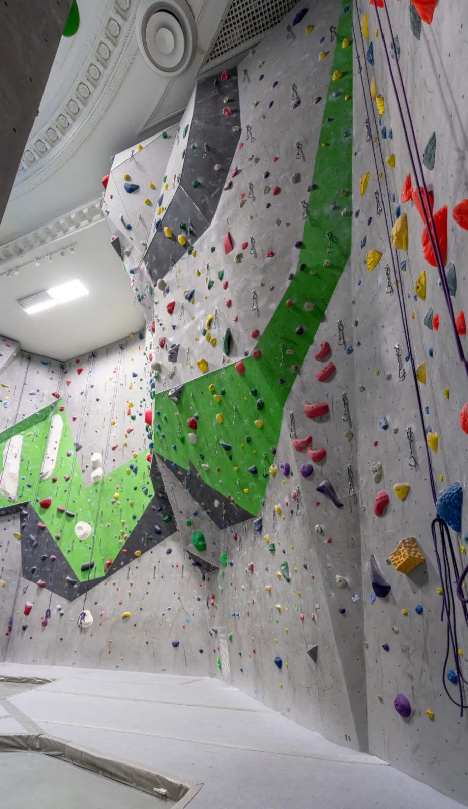 Looking up a high climbing wall with ropes towards the old cinema's decorative ceiling