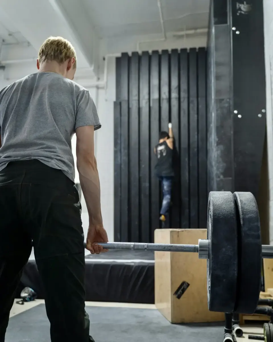 Climber on the black crack-climbing wall, with a loaded barbell in the foreground