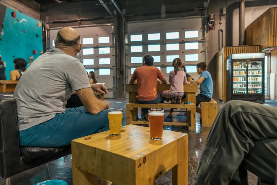 Two beers on a wooden table in the bistro area, with a drinks fridge and the climbing wall behind