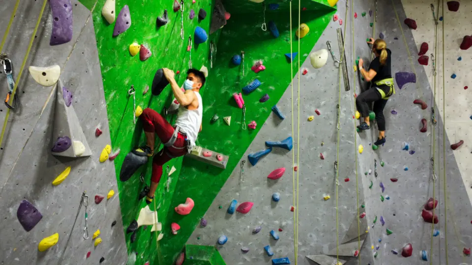 Two climbers on green and grey roped walls with quickdraws