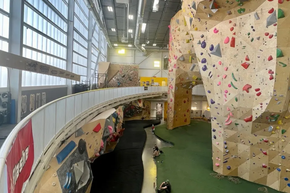Tall roped climbing towers beside a curved mezzanine above the bouldering wall