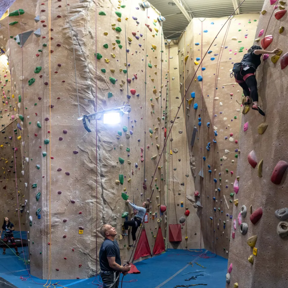 Climbers on top-rope routes up tall walls, with a belayer watching from the floor