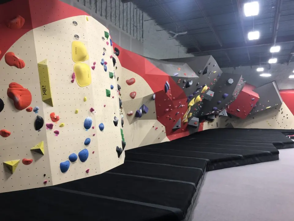 Long red, grey and cream bouldering wall with overhangs above thick black matting