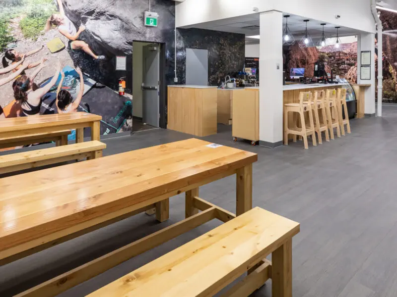 Lounge with wooden tables and benches beside a café counter with bar stools