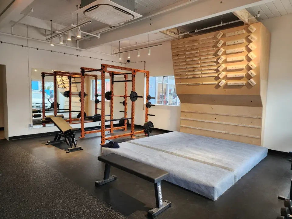 Fitness room with orange power racks, a weight bench and a wooden campus board above a mat