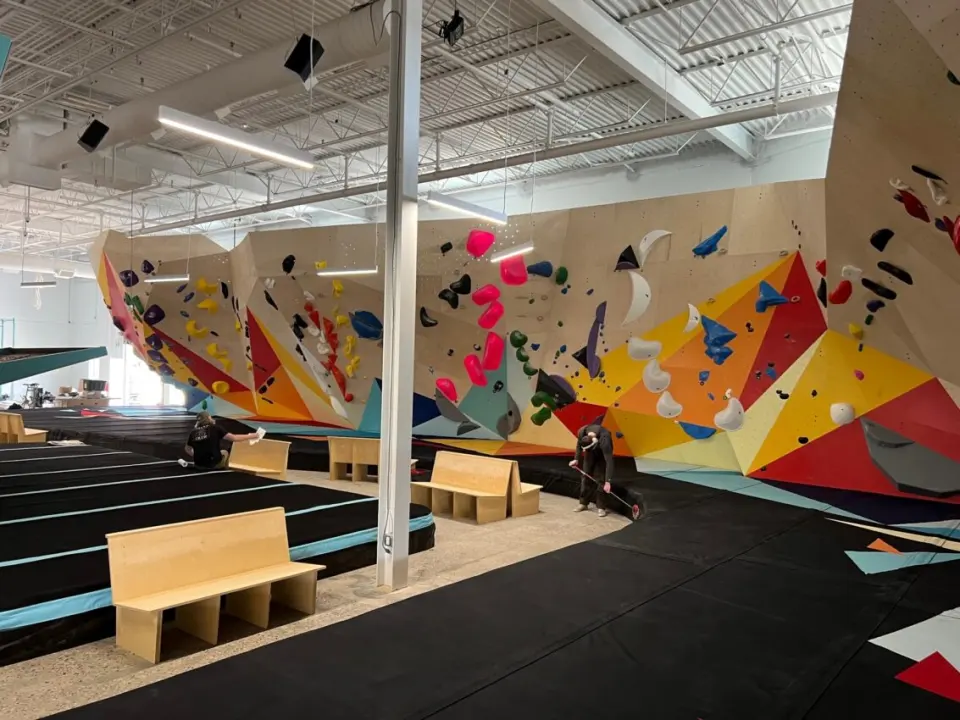 Long bouldering wall painted in bold triangles, with wooden benches on the matting