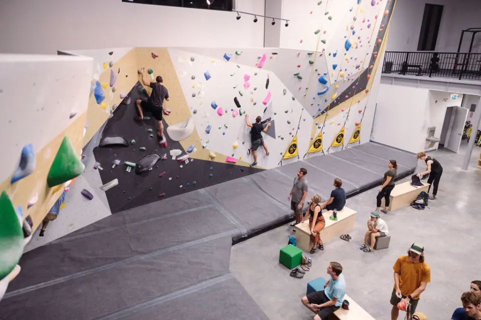 Climbers on an overhanging wall while others rest on benches below