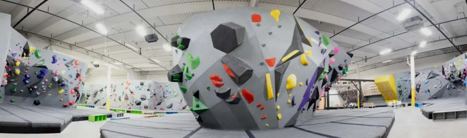 Panorama of the bouldering hall around a freestanding boulder, with the training area behind